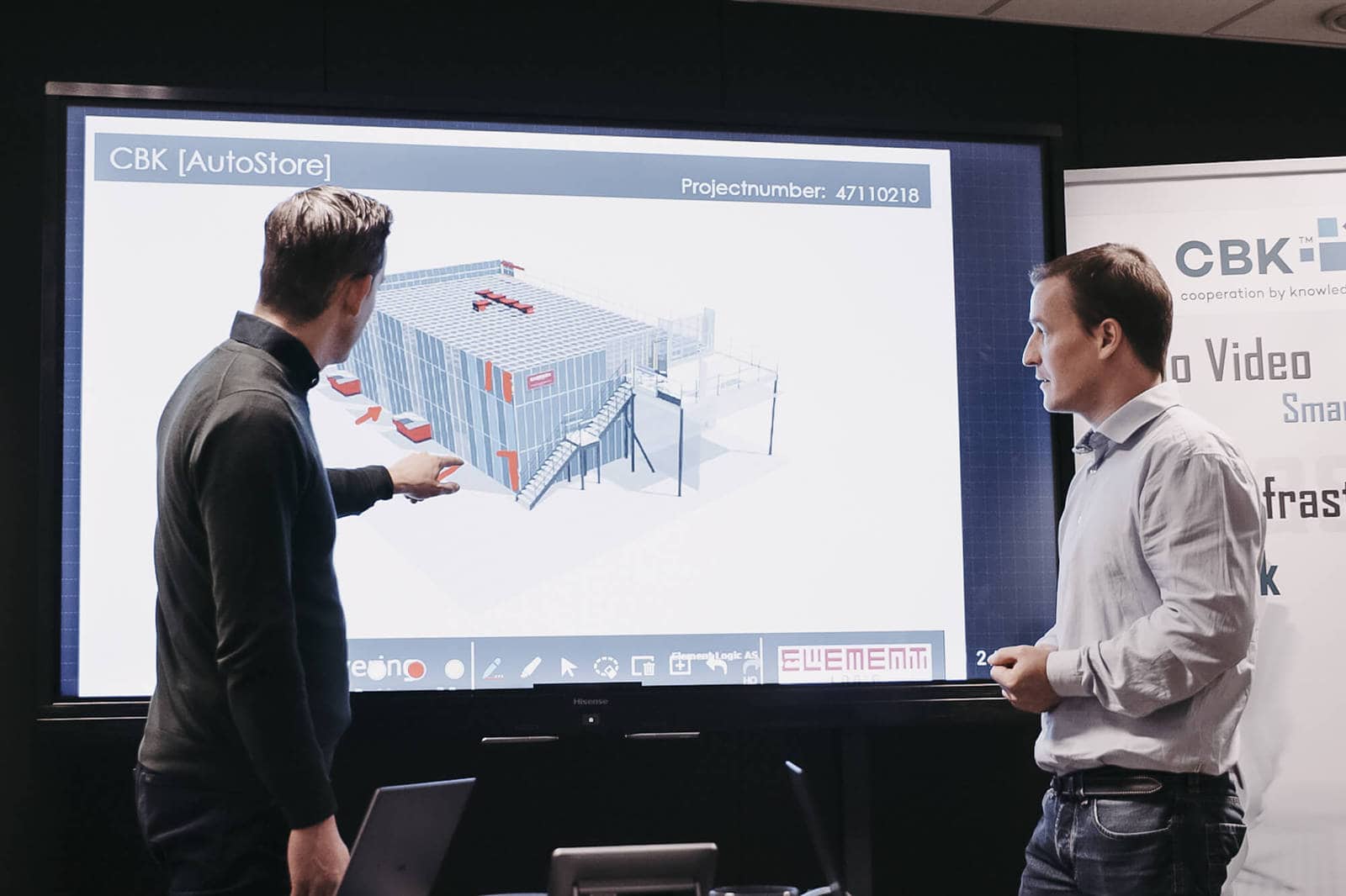 Dwóch mężczyzn wskazuje i patrzy na prezentację rysunku rozwiązania AutoStore.