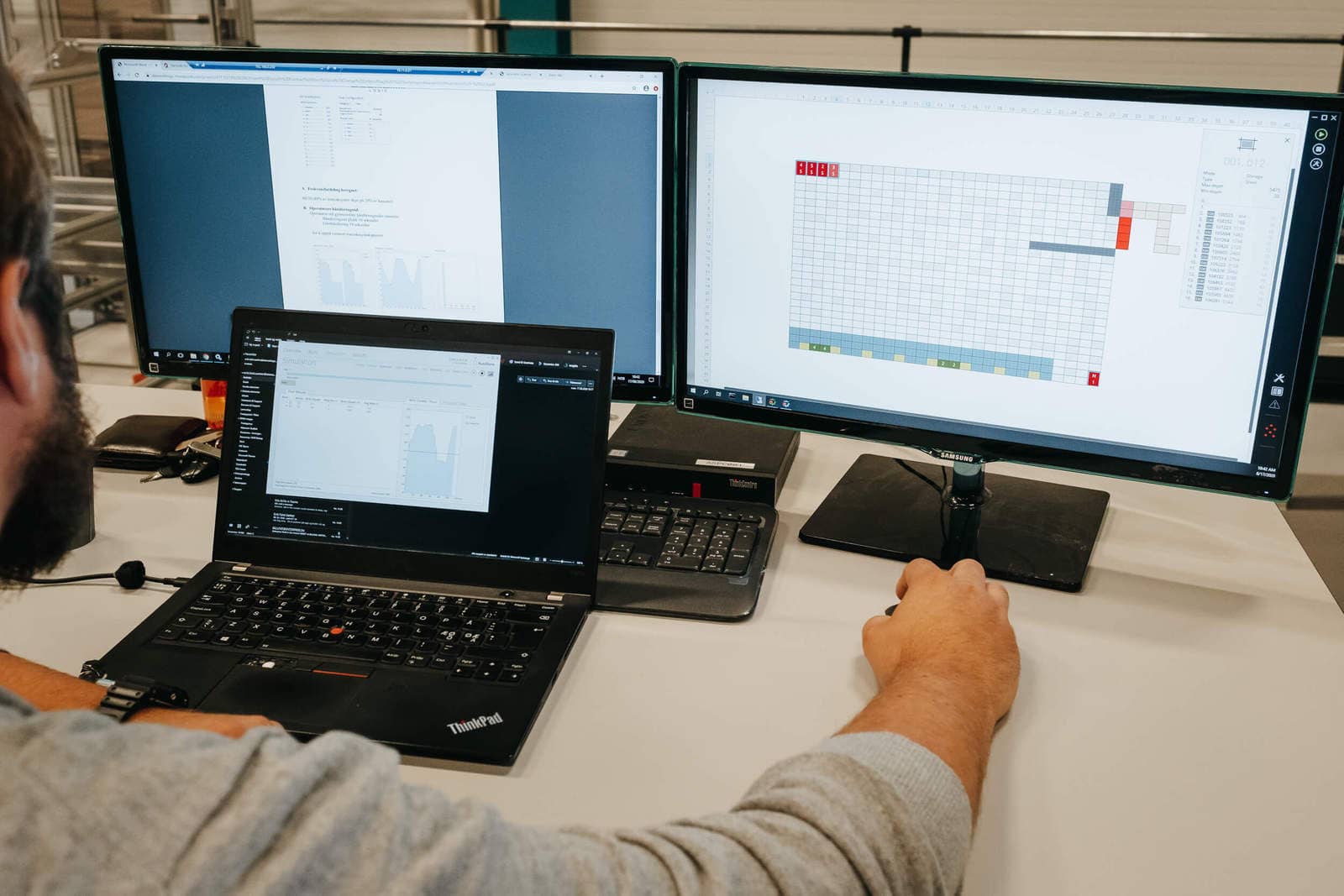 Mężczyzna pracujący przy AutoStore przy trzech ekranach komputerowych.