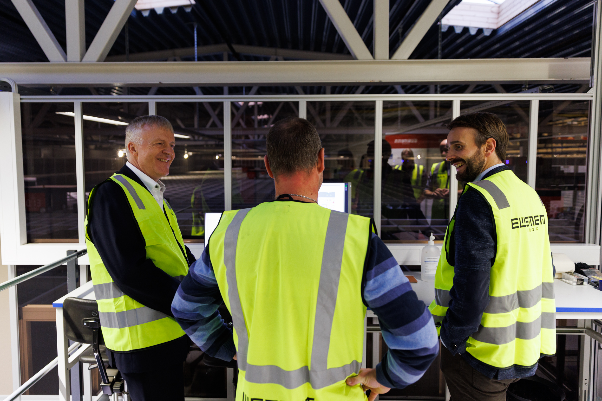 Minister handlu i przemysłu rozmawia z Dag-Adler Blakseth i Lasse Vik, którzy z antresoli spoglądają na siatkę AutoStore